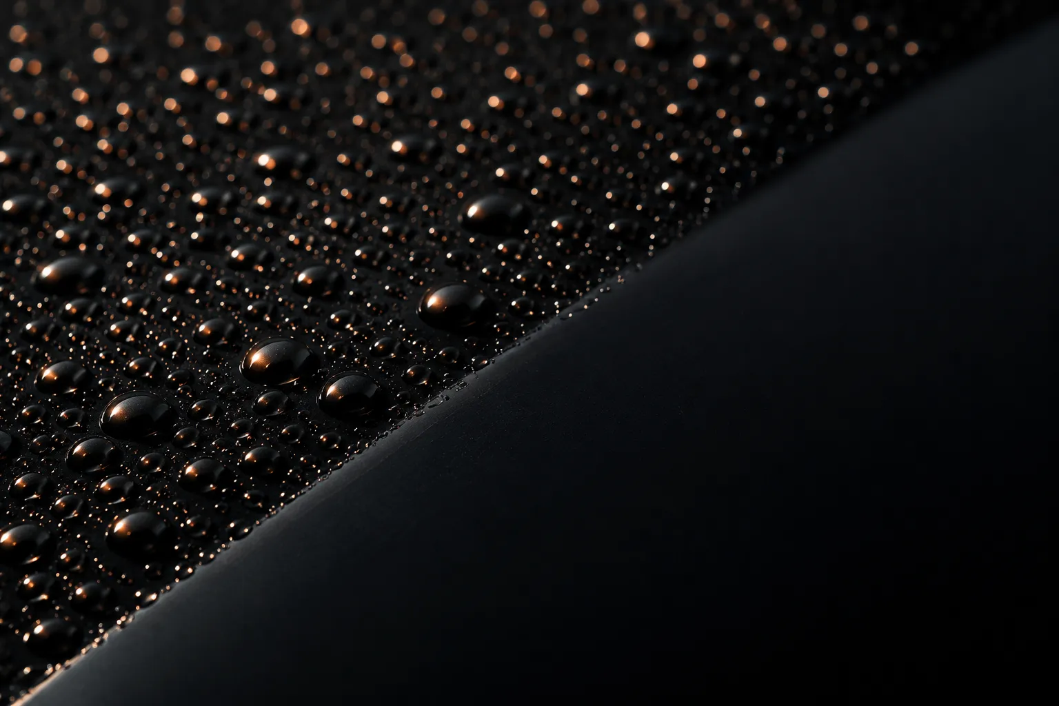 Water beading on black paint, cut by a clean diagonal wiped edge