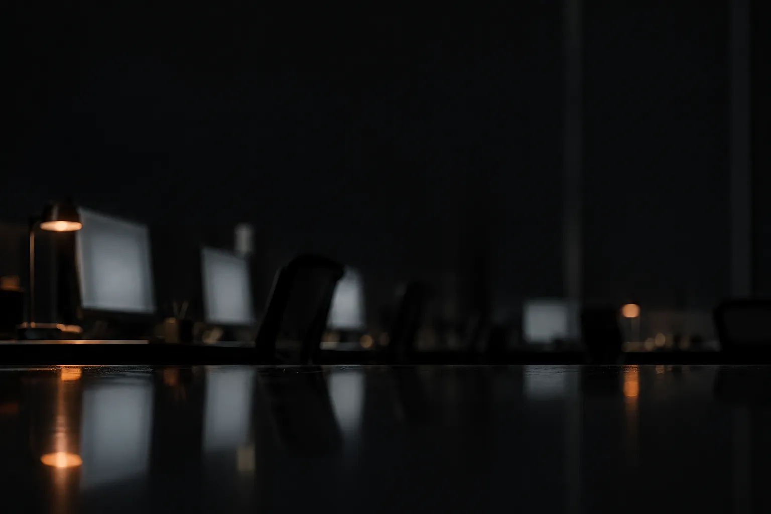 Reflections of a dark office at night on a black glass desk